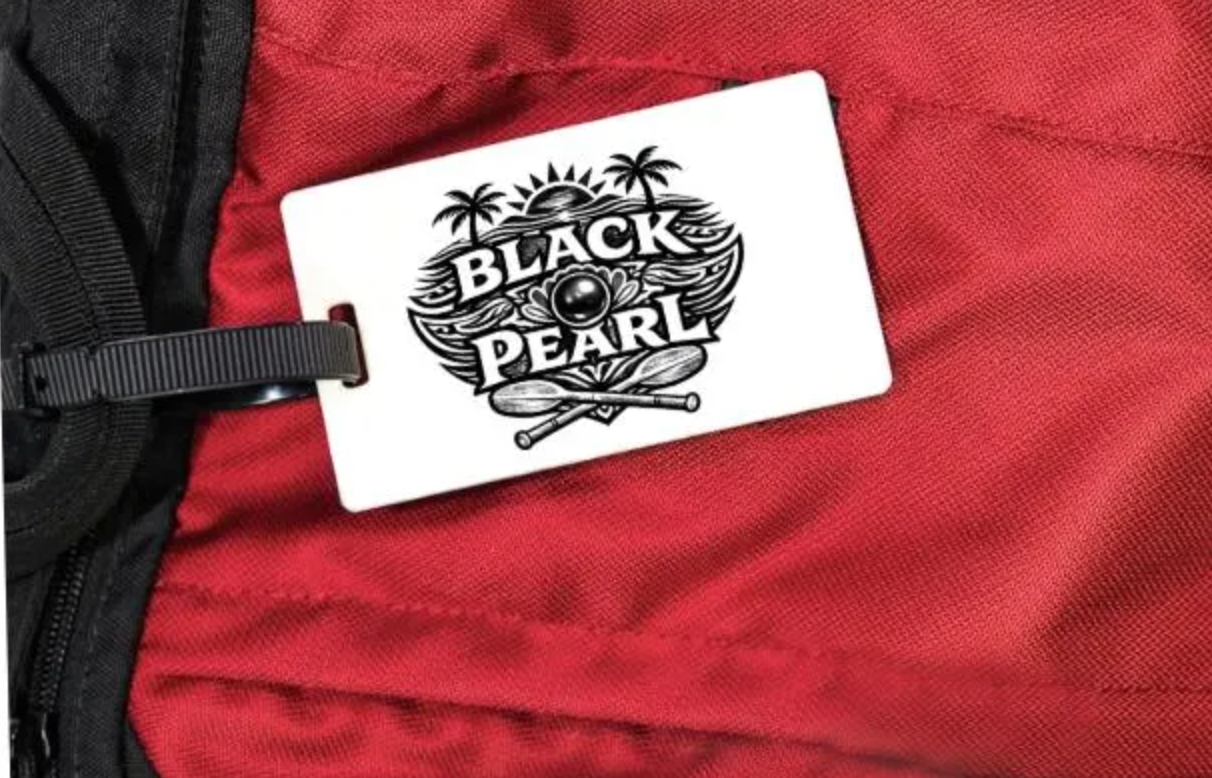 White luggage tag with 'Black Pearl' design attached to a red bag.